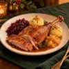 produkt-portion-brust-v4-ki-klein Gänsebratenportion mit Keule und einem Stück Gänsebrust, Apfelrotkohl, zwei Kartoffelknödeln, Apfelkompott und Sauce – KI-generierte Illustration.